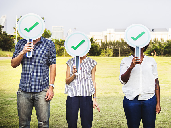 Three people stand in front of a lawn and hold voting paddles with the acceptance symbol. The paddles cover their faces