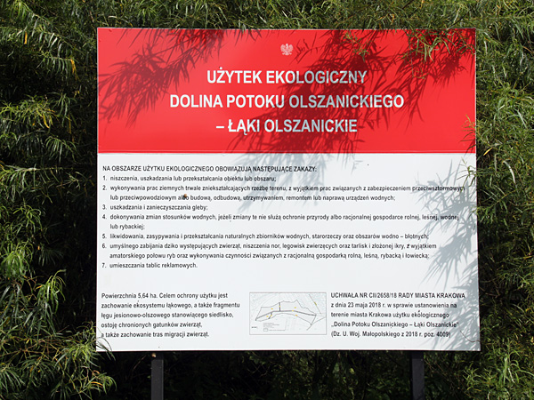 A large red and white board with detailed text explanations standing against the background of a clump of trees or shrubs