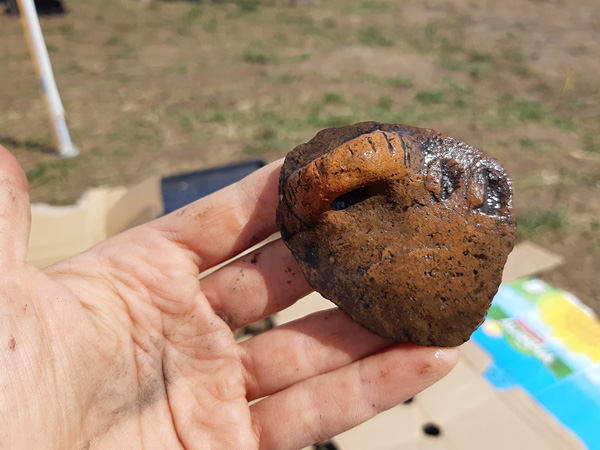 A hand holding a fragment of a clay vessel with a preserved ear