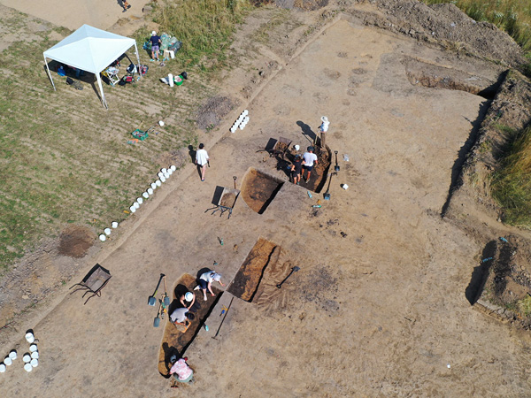 View from above of a group of people digging soil out of holes. A tent stands next to the excavation site