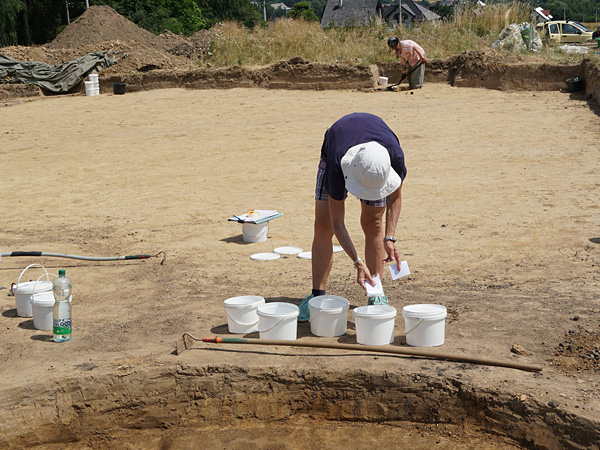 A woman in a white hat leans over white plastic buckets