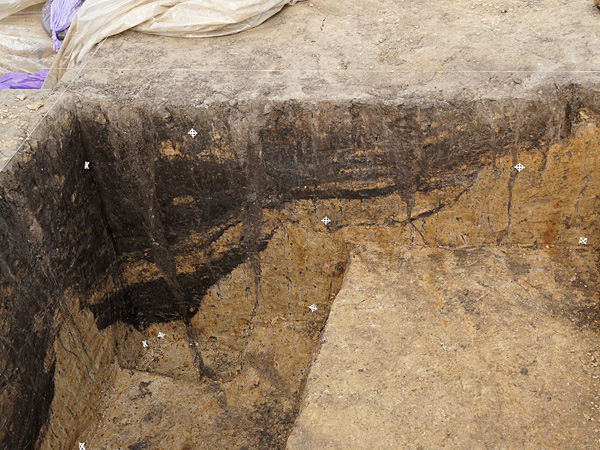 A deep hole with vertical walls, with a clearly visible soil profile. The soil is black at the top and yellow at the bottom