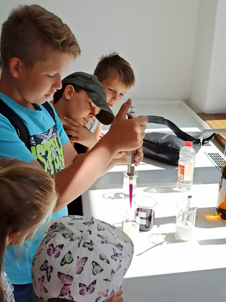 A boy uses a pipette to measure out a portion of purple liquid. His friends watch what he does