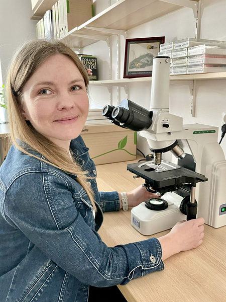 Smiling blonde woman in denim jacket sits at microscope