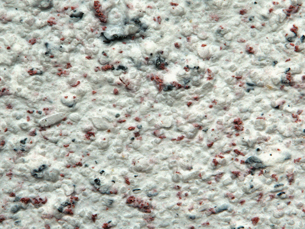 A bright, rough surface resembling plaster with red and black particles embedded in it