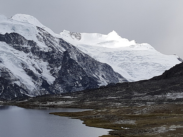 A rugged high-mountain landscape. A pond in the foreground, rocky snow-capped peaks in the background