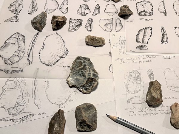 Pencil and flint tools lie on several sheets of paper with numerous sketches of these tools