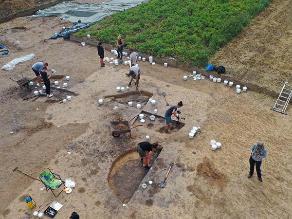 View from above of shallow holes where several people are working, digging or collecting samples into white plastic buckets