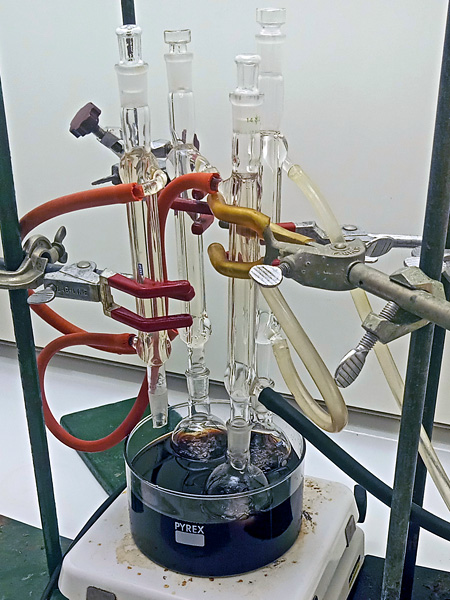 Glass laboratory vessels fixed in holders, immersed at the bottom in a beaker with a black liquid standing on a heater