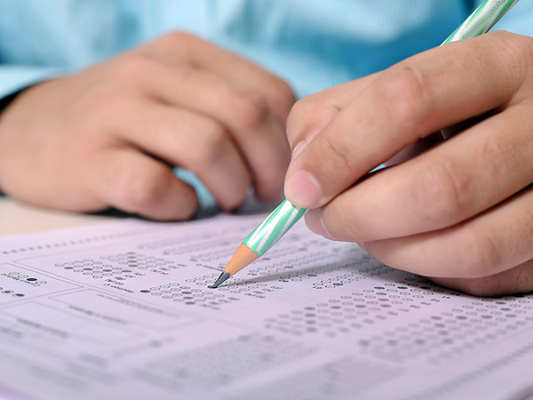 Close-up of a student's hand holding a pencil and marking answers on a white multiple choice test sheet