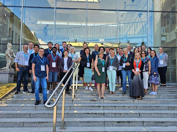 A large group of people pose for a photo while standing on the steps in front of the glass wall of a university building