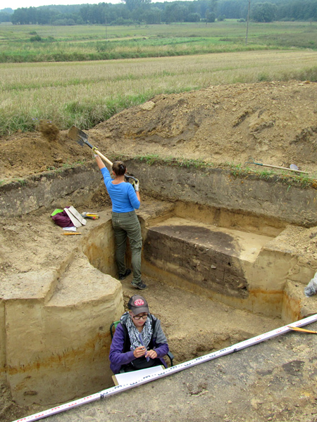 Two women in a hole of complicated geometry. One shovels earth out of the hole, the other sketches something