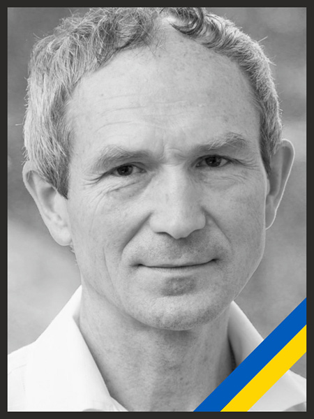 A black and white photo of a man with a friendly look, girded with a blue and yellow sash, the colors of the Ukrainian flag