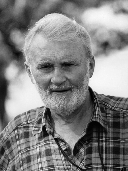 A black and white photo of an older man with white hair and beard, wearing a plaid shirt