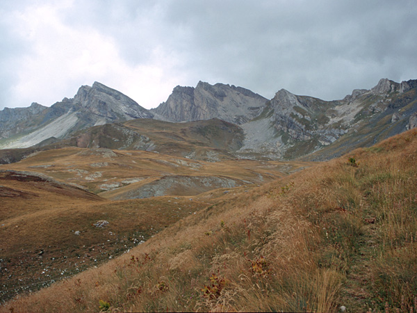 Gently undulating slopes covered with yellow grass. In the background, a range of sharp, rocky mountain peaks