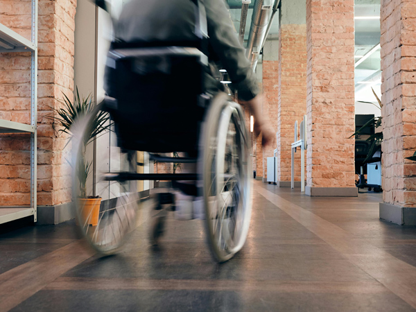 A rear view of a person in a wheelchair moving through a hallway lined with brick walls and columns