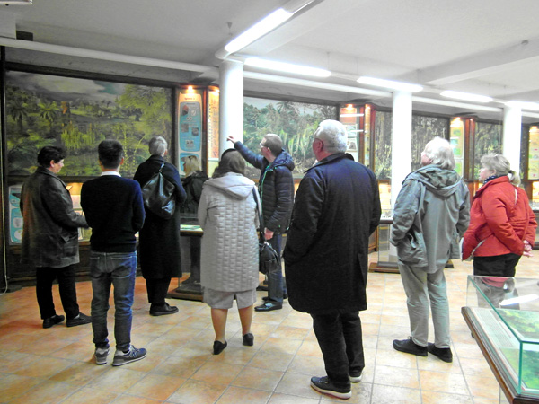 A man points to the illustrations hanging on the walls. A group of people surround him, listening