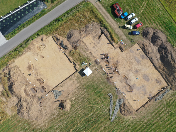 Aerial view of two rectangular fields without topsoil. Next to them is a street and parked cars