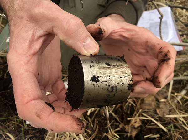 Dirty male hands hold a small metal cylinder filled with black soil and smeared on the outside