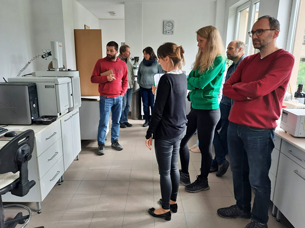 A group of people explore a bright laboratory room. White cabinets and scientific equipment line the walls