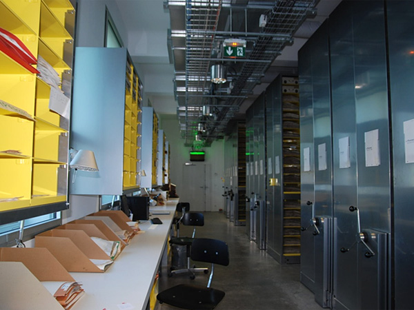 A long room with metal rolling archive shelves on one side and a row of tables and chairs on the other