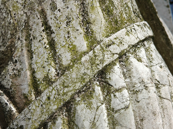 A fragment of a white stone sculpture covered with a green coating, especially in the grooves