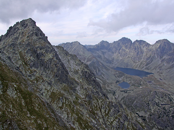 High mountain landscape. On the left, high, gray, rocky peaks, on the right, in the distance, the surfaces of mountain ponds